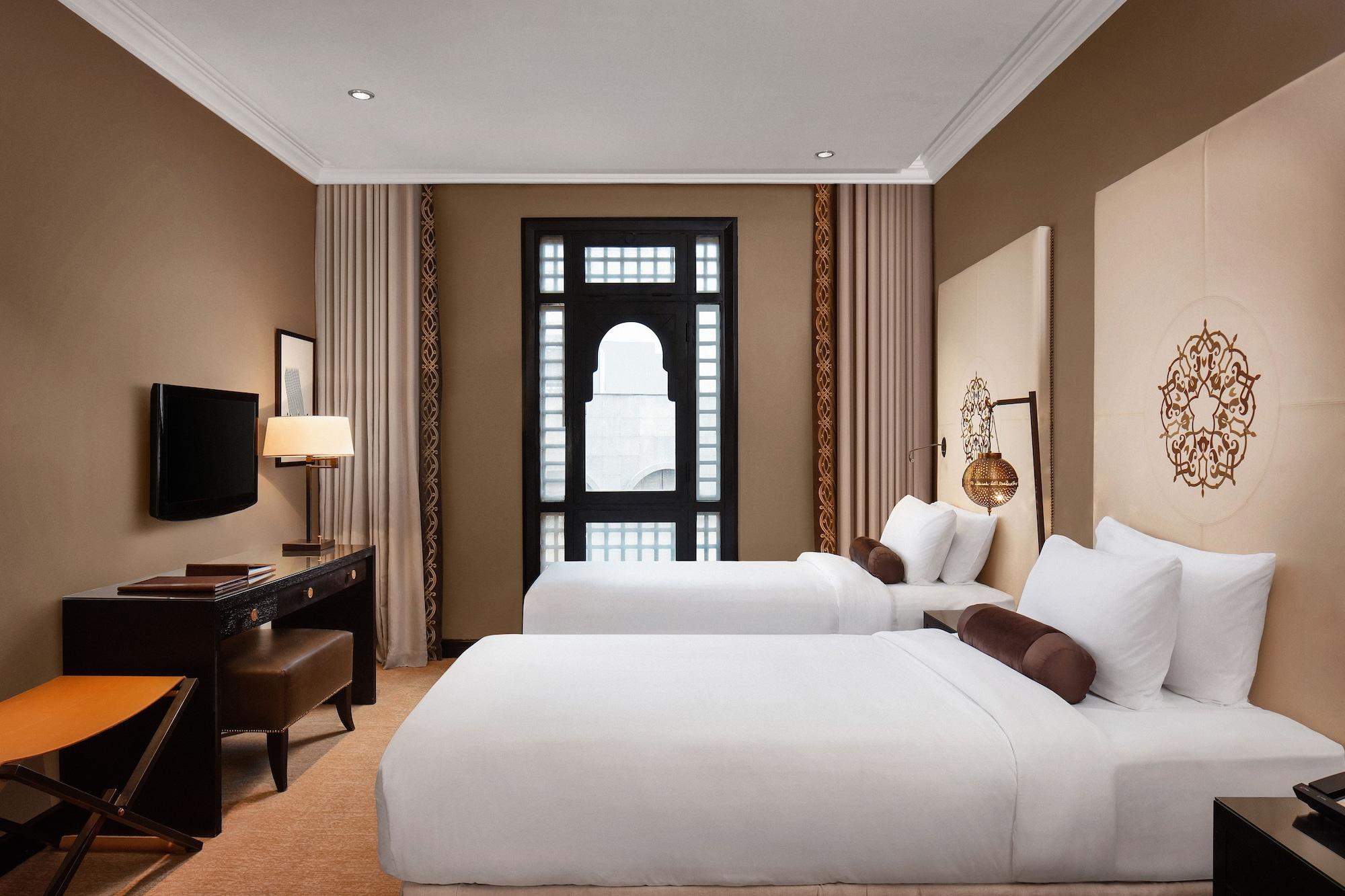 Sofitel Shahd Al Madinah Otel Medine Dış mekan fotoğraf The photo shows a well-decorated hotel room featuring two single beds with white bedding. The walls are a warm beige color, and there are decorative elements such as patterned wall panels and a large window with an elegant design. In the room, there 