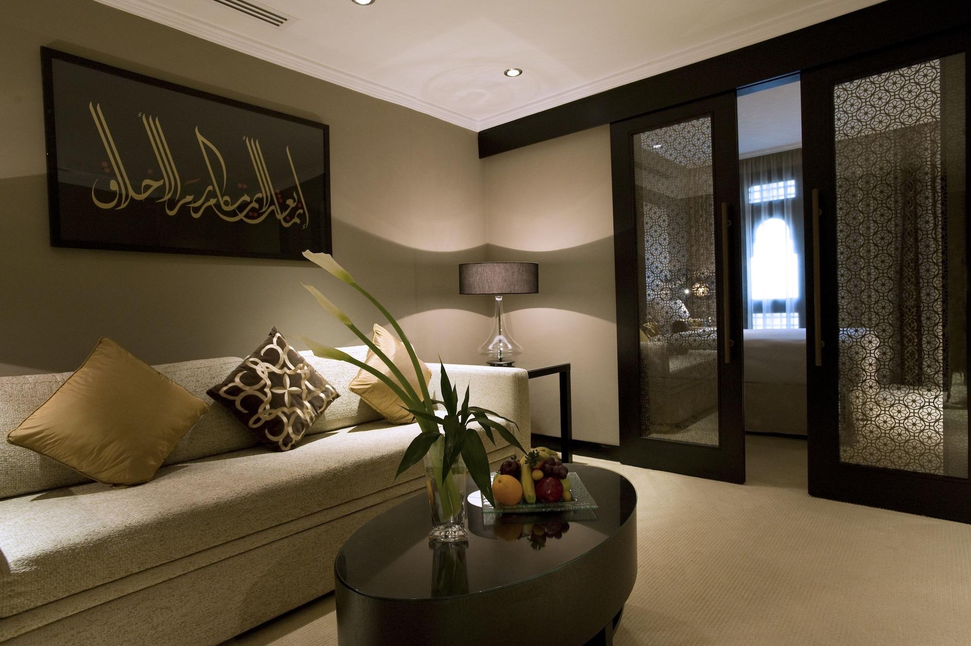 Sofitel Shahd Al Madinah Otel Medine Dış mekan fotoğraf The photo shows a modern and elegantly designed lounge area. There is a light-colored sofa adorned with decorative cushions. A sleek, dark coffee table sits in front of the sofa, topped with a small vase containing flowers and a fruit arrangement. To