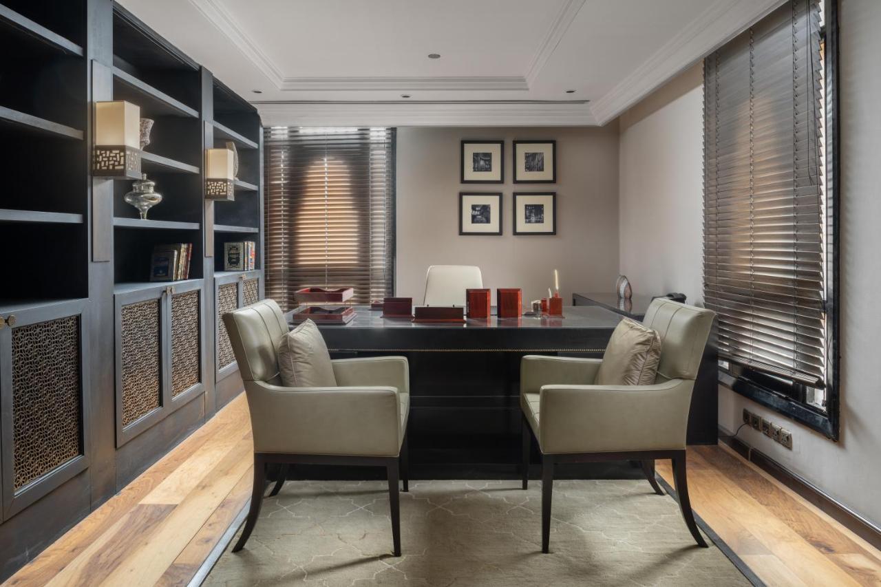 Sofitel Shahd Al Madinah Otel Medine Dış mekan fotoğraf The photo depicts a modern office space. It features a large, dark wooden desk at the center, with two matching chairs positioned in front of it. Behind the desk is a minimalist white chair. The walls are adorned with framed pictures and there are bu