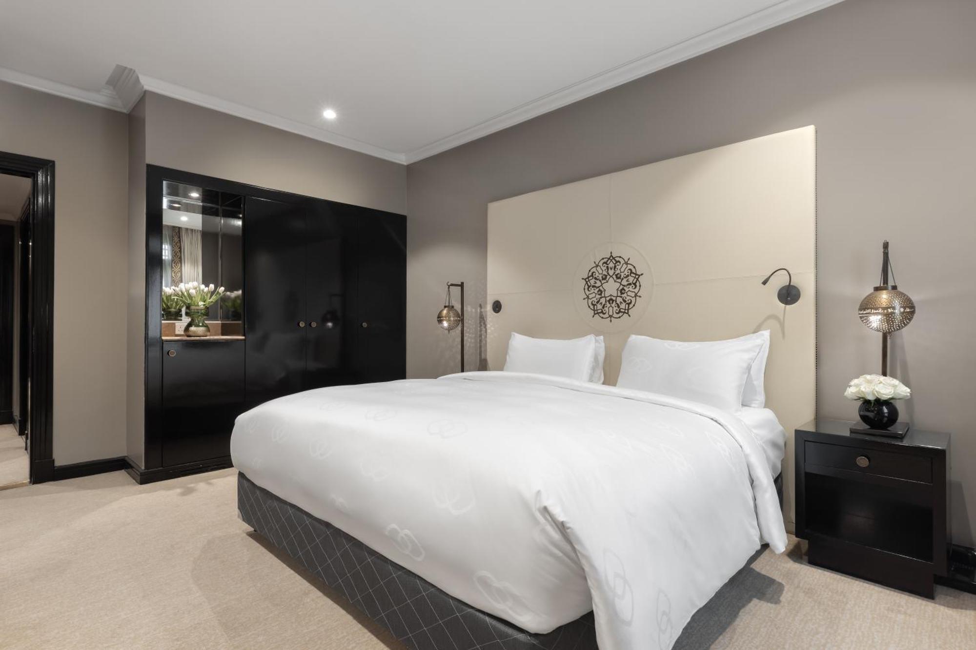 Sofitel Shahd Al Madinah Otel Medine Dış mekan fotoğraf The photo displays a modern and stylish bedroom. It features a large bed with white linens and two pillows, placed against a light-colored wall with an elegant headboard design. On each side of the bed, there are bedside tables with lamps that add a 