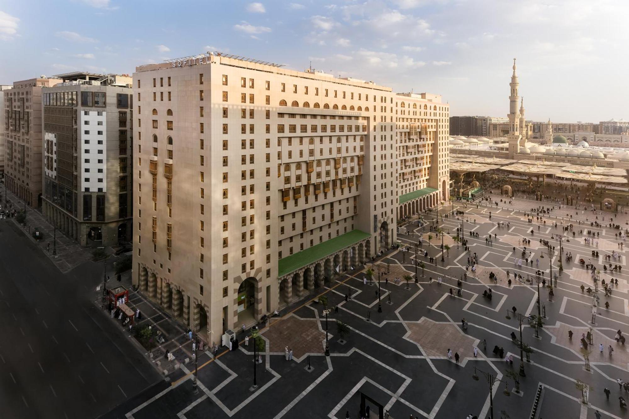 Sofitel Shahd Al Madinah Otel Medine Dış mekan fotoğraf The photo shows a large, multi-story building with a distinct architectural design, located near a spacious outdoor plaza. The building features a combination of columns and large windows, giving it a formal appearance. In front of the building, ther