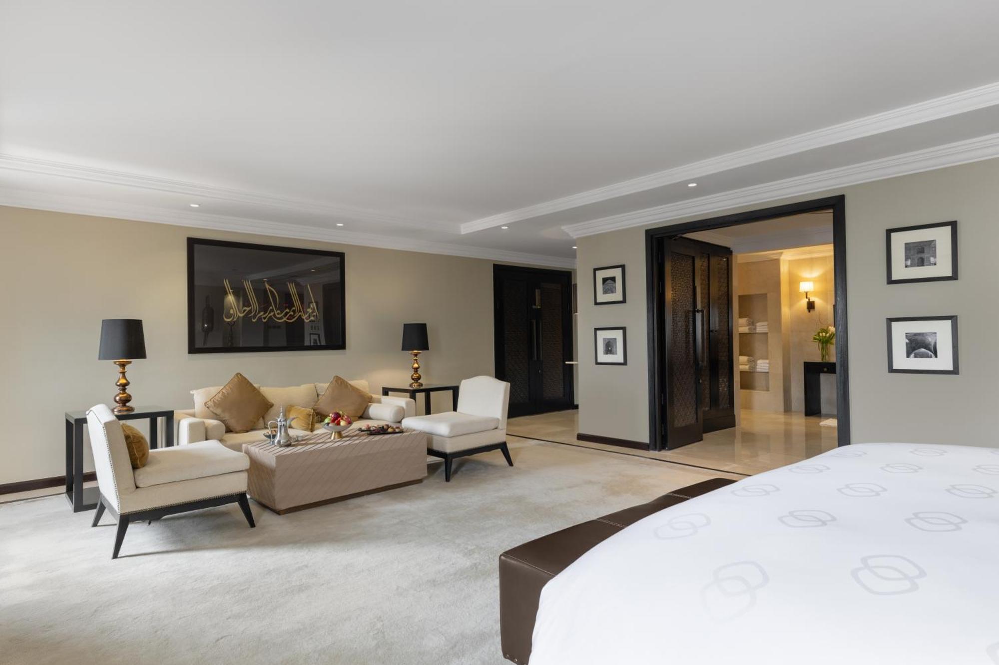 Sofitel Shahd Al Madinah Otel Medine Dış mekan fotoğraf The photo depicts a spacious and elegantly designed hotel suite. In the foreground, there is a large bed with a dark headboard. To the right of the bed, there is a plush carpeted area. 

In the living area, there are two light-colored armchairs and a