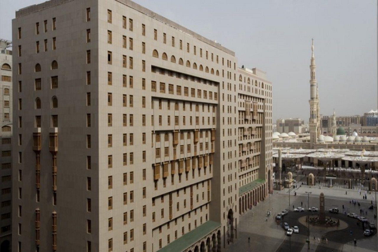Sofitel Shahd Al Madinah Otel Medine Dış mekan fotoğraf The photo shows a large modern building with a facade that features numerous windows and architectural detailing. It is situated in an urban setting, with another prominent structure, likely a mosque or minaret, visible in the background. The surroun